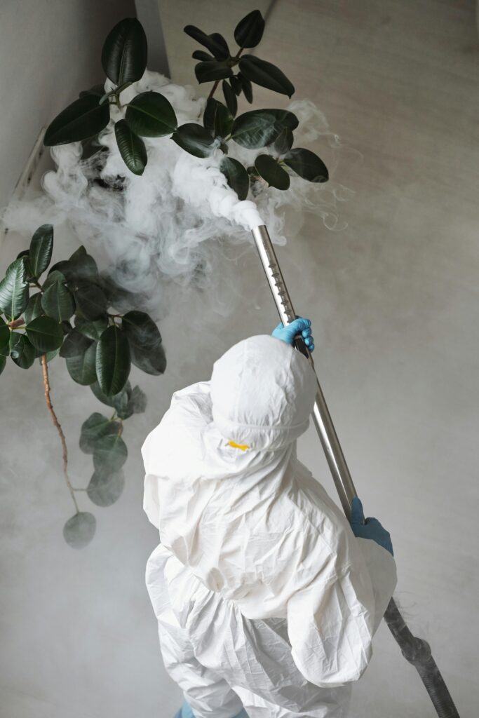 pexels-photo-4176550-4176550 A person in protective gear uses a sprayer for indoor disinfection.
